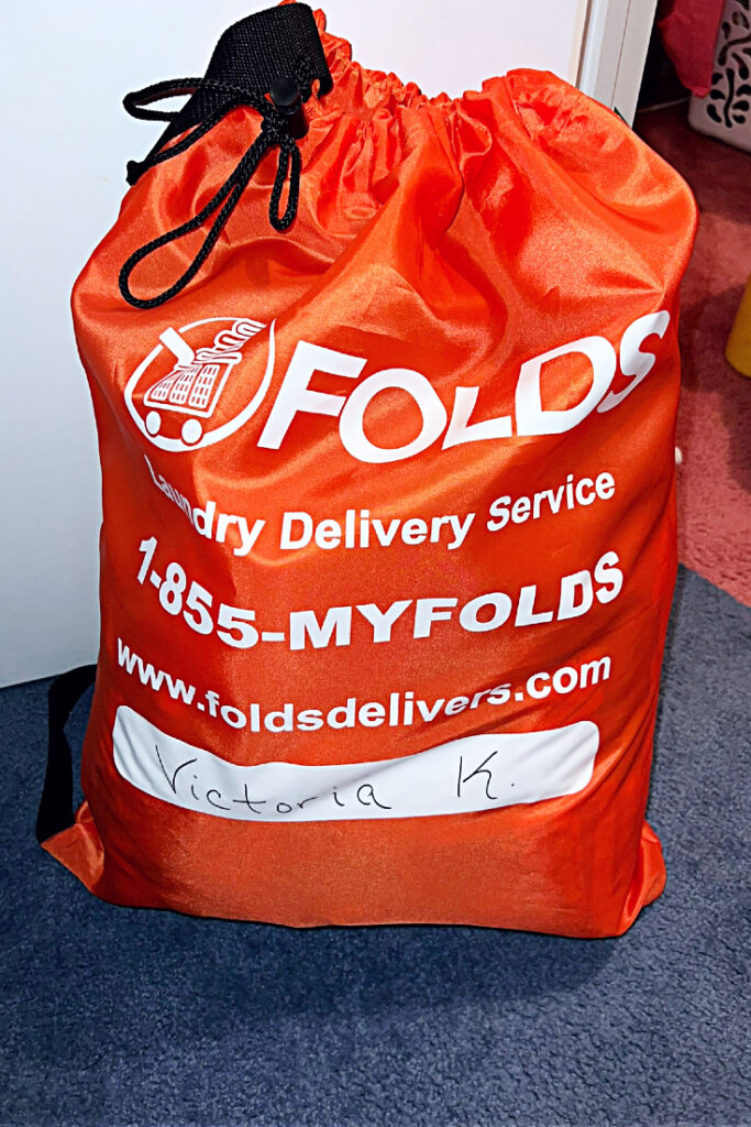 orange tied bag of FOLDS laundry, laundry delivery service with packaged clean clothes inside