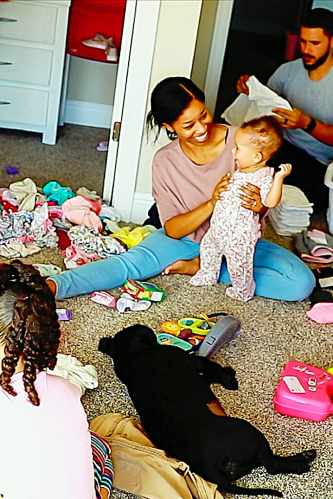 huge pile of clothes and toys on the floor as Victoria Vaden, lazy wife and husband fold together with daughter, baby girl and small dog