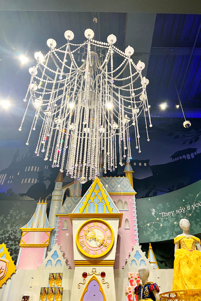 Victoria Vaden captured image of Times Square Disney Story with a large, illuminated chandelier above a beautiful pink, yellow and green princess castle on the sales floor.
